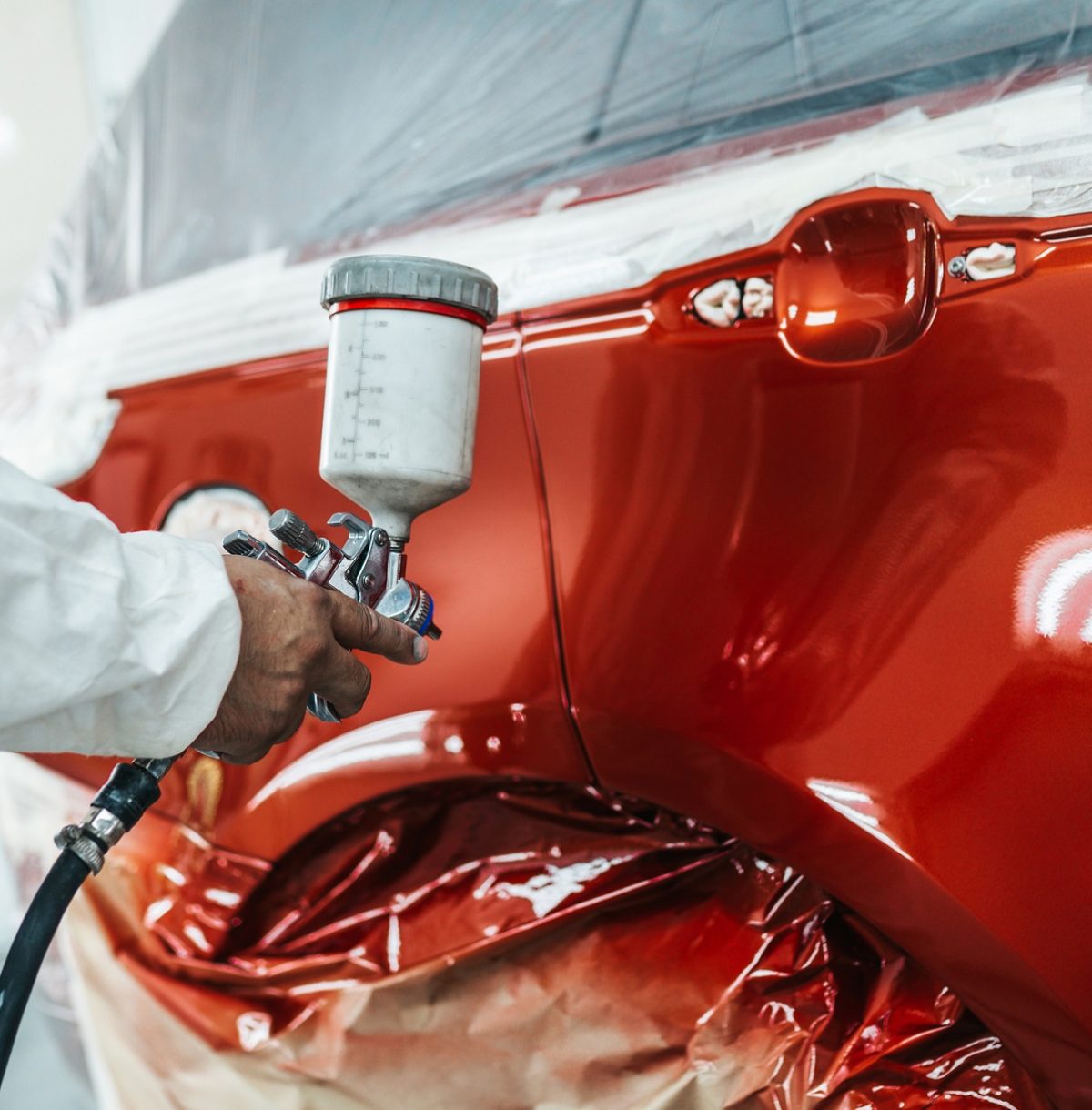 Man with protective clothes and mask painting car using spray compressor.